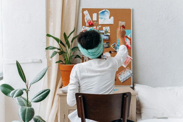 A woman in a cozy room organizing a vision board with photos and ideas.
