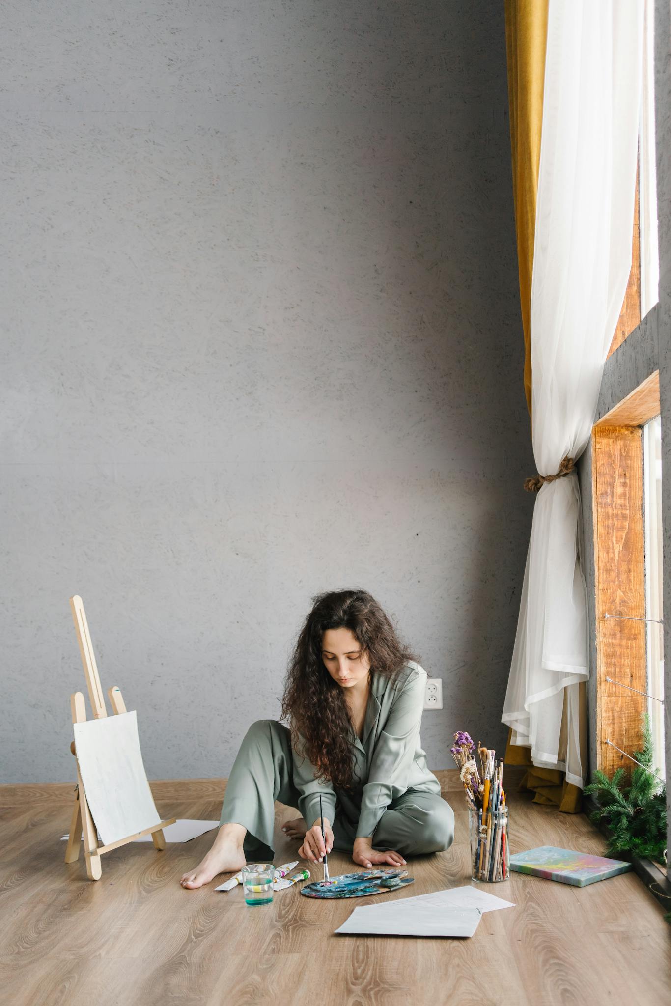 A young woman in casual attire painting on the floor of a modern studio with natural light.
