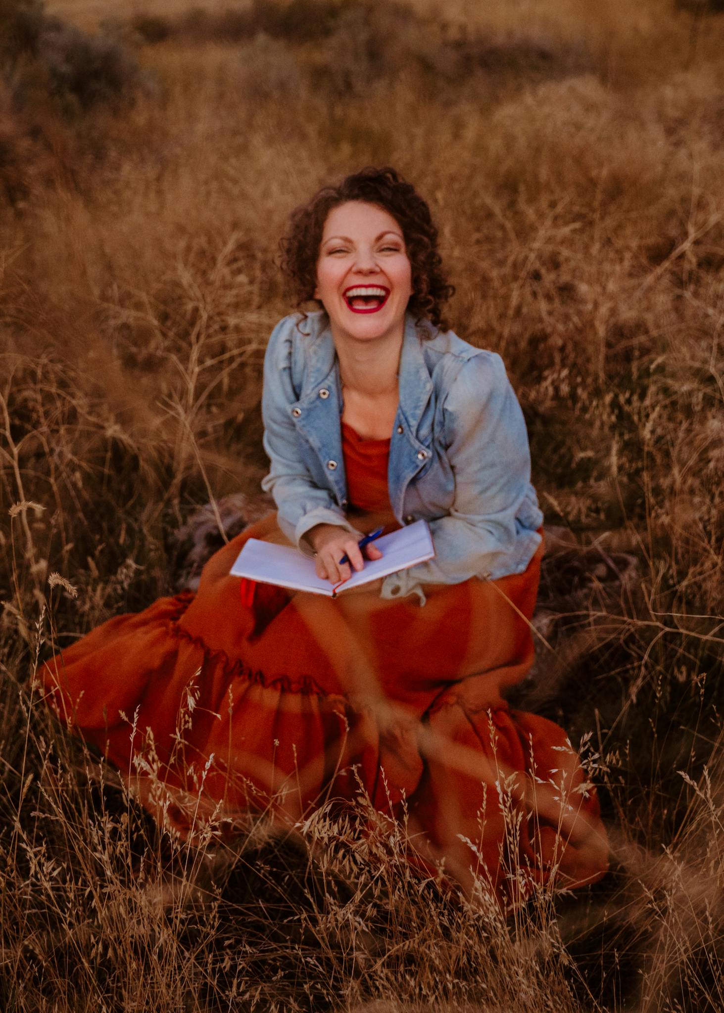Happy woman sits in a meadow journaling, embracing self-care and joy.